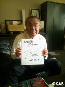サインを手に満面の笑みの会長